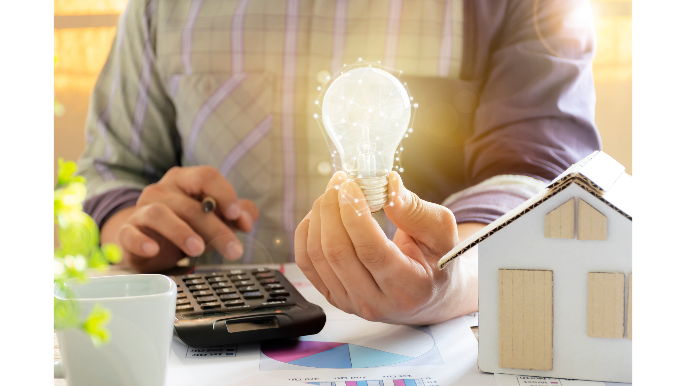 man sitting at desk with light bulb, calculator, and model house
